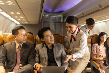 Two businessmen using computer notebook to connect and check their work in an airplane cabin before boarding. Airline crew is helping travelers to enjoy internet connection during a flight