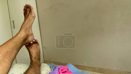 Téléchargez les photos : La jambe d'un Asiatique. Pied Crossover relaxant sur le lit avec garde-robe blanche sur le fond - en image libre de droit