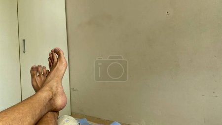 Téléchargez les photos : La jambe d'un Asiatique. Pied Crossover relaxant sur le lit avec garde-robe blanche sur le fond - en image libre de droit