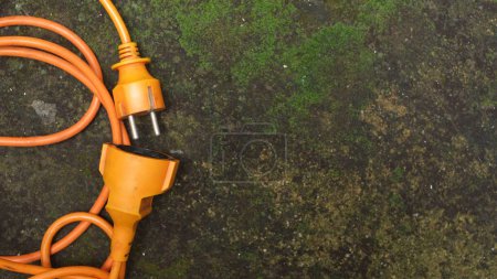 Photo for Messy bright orange extension cord. Orange extension cable on mossy concrete floor - Royalty Free Image