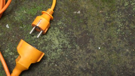 Photo for Messy bright orange extension cord. Orange extension cable on mossy concrete floor - Royalty Free Image