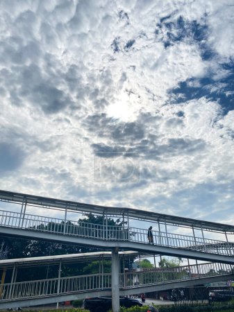Photo for Unrecognized senior man crossing a pedestrian bridge with against cloudy blue sky. - Royalty Free Image