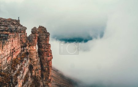 Soft focus. Awesome caucasus landscape with silhouette of hiker above white clouds and Rocks of Big Bermamyt - the so-called "Monks".  Man with backpack in high mountains. Panoramic view. 