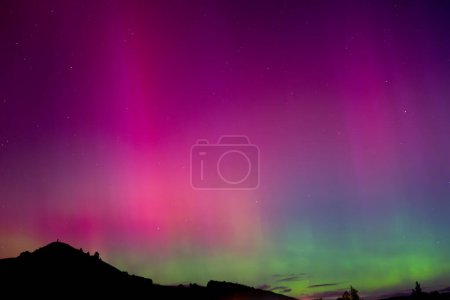 Pink and green Aurora Australis over Puketapu mountain in Palmerston, Otago. Palmerston is located in the South Island of New Zealand, where the southern lights can be seen. 