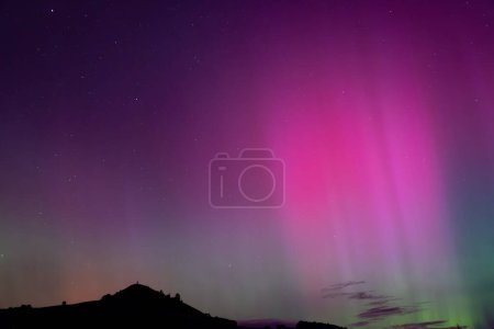 Aurora Australis with pink beams over Puketapu mountain in Palmerston, Otago. Palmerston is located in the South Island of New Zealand, where the southern lights can sometimes be seen. 
