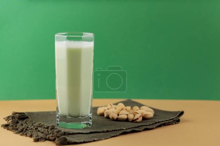 Photo for Pistachio milk in the glass on a dark green linen napkin. Lactose free pistachio milk and scattered pistachios. Copy space - Royalty Free Image