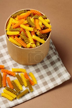 Téléchargez les photos : Pâtes sèches Fusilli sur une serviette en lin. Pâtes fusilli vertes, oranges et jaunes en boîte écologique. Cuisine italienne - en image libre de droit