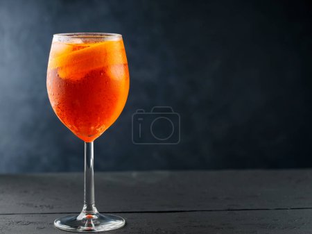 Aperol Spritz cocktail in glass with fresh orange on dark wooden boards. Glass of Aperol Spritz cocktail served in a wine glass. Copy space