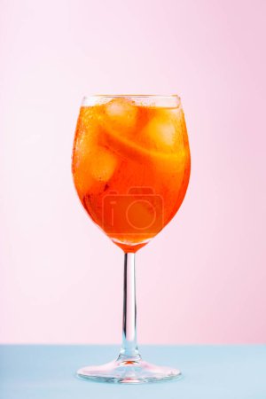 Aperol Spritz cocktail in glass on a pink blue background. Cocktail Aperol Spritz with orange and ice cubes. Close up