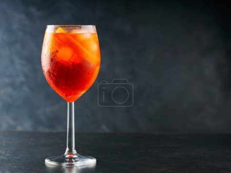 Aperol Spritz cocktail in glass with fresh orange on dark background. Glass of ice cold Aperol Spritz cocktail served in a wine glass. Copy space