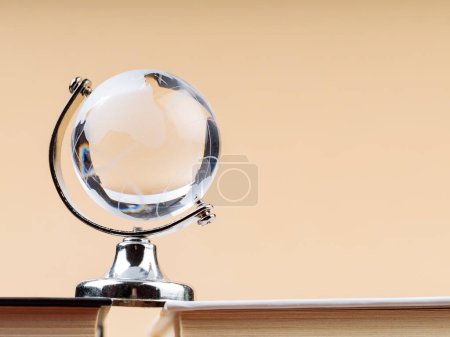 Glass Globe on Stack of Books on Beige Background, Fragile Balance of Earth's Ecosystem
