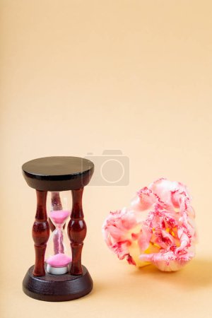 Hourglass and Fading Flower Petals on Beige Background, Concept of Urgency to Solve Environmental Problems, Copy Space