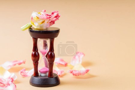 Hourglass and Fading Flower Petals on Beige Background, Concept of Urgency to Solve Environmental Problems, Copy Space