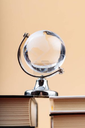 Glass Globe on Stack of Books on Beige Background, Fragile Balance of Earth's Ecosystem