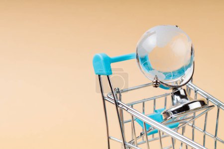 Shopping Cart with Glass Globe on Beige Background, World Trade Concept, Copy Space