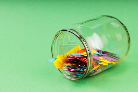 Glass Jar Filled with Colorful Paper Scraps on Green Background, Concept of Reducing Paper Waste Through Recycling