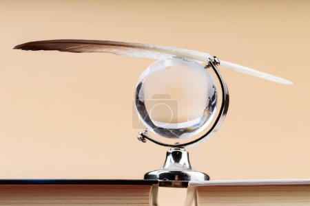 Glass Globe with Balancing Bird Feather on Stack of Books, Fragile Balance of Earth's Ecosystem Concept