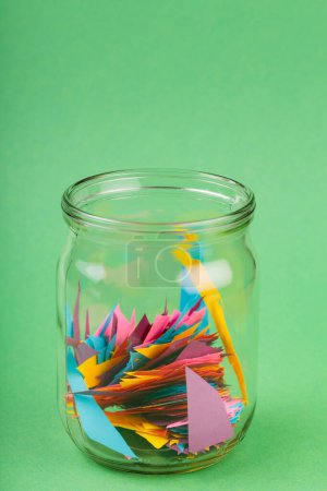 Glass Jar with Colorful Paper Scraps on Green Background, Recycling Concept