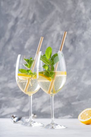 Hugo Spritz Cocktail in Glass Garnished with Mint and Lemon with Bamboo Straw on Concrete