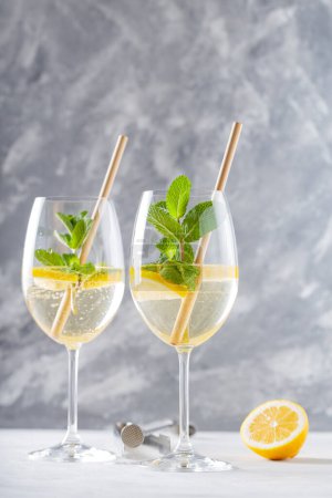 Hugo Spritz Cocktail in Glass Garnished with Mint and Lemon with Bamboo Straw on Concrete