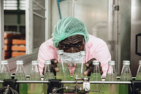 Téléchargez les photos : Le personnel nigérian africain travaille dans le contrôle de la qualité de l'usine de boissons à la ligne de produits de bande transporteuse - en image libre de droit