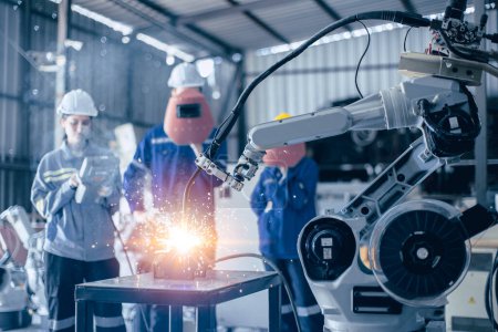 Téléchargez les photos : Le contrôle de travail de l'équipe d'ingénieurs opère un petit bras de soudage robotisé dans un atelier de métal - en image libre de droit