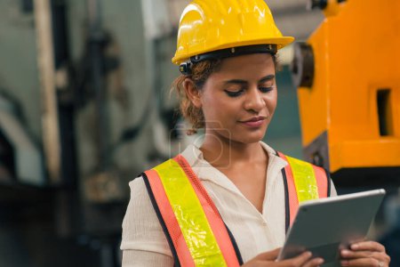 Foto de Happy African American Woman Engineer Worker Supervisor mirando la computadora Tablet para controlar operar el mecanizado en Heavy Industry Factory. - Imagen libre de derechos