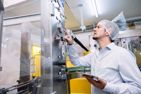 Foto de Máquina automática de configuración de trabajo masculina de ingeniero en fábrica de la industria de bebidas alimenticias. - Imagen libre de derechos