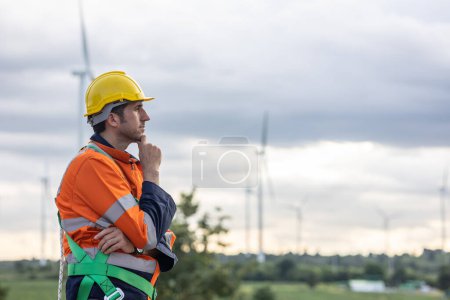 Foto de Ingeniero profesional trabajador masculino de pie pensando mano a mano en la barbilla en el campo de aerogeneradores trabajando - Imagen libre de derechos