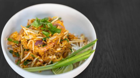 Photo for Pad thai coriander on top juicy creamy tasty delicious world popular. Thai famous food menu closeup in bowl on black wood table. - Royalty Free Image