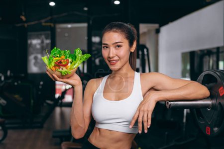 Photo for Sport healthy beautiful asian woman showing vegetables mix salad for diet food low calories in fitness sport club - Royalty Free Image