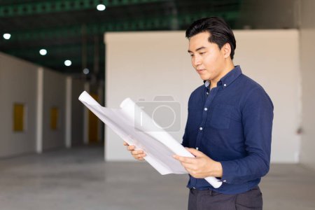 Photo for Asian engineer business architect male standing in factory building with floorplan blueprint construction design project - Royalty Free Image