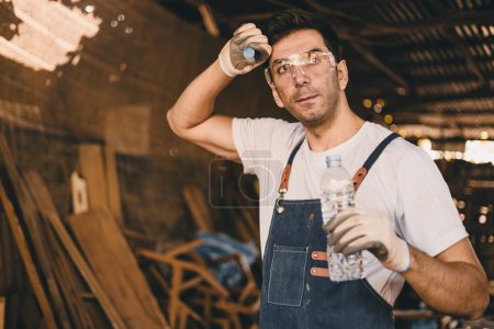 Photo for Tired stress carpenter man worker sweating hot workplace hardwork drinking water brake relax dehydrate in wood furniture workshop. - Royalty Free Image