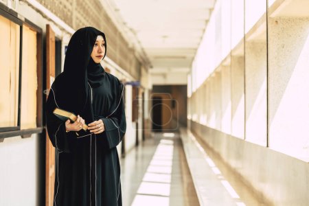 Téléchargez les photos : Jeune niqab musulmane adolescente lisant le Coran et la foi Le Saint Coran dans un bâtiment de l'Université. arabe noir tchador dame. - en image libre de droit