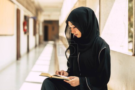 Young teen muslim niqab woman reading the Quran and faith The Holy Al Quran in University building. Arab black chador lady.
