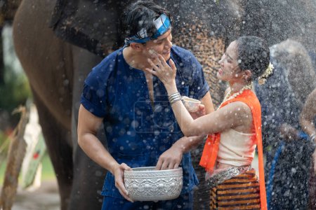 Téléchargez les photos : Festival de Songkran. Peuple thaïlandais du Nord en vêtements traditionnels s'habiller éclaboussant l'eau ensemble dans le festival culturel de jour de Songkran avec fond d'éléphant. - en image libre de droit