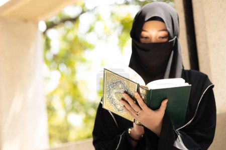 Photo for Muslim niqab woman read and learning the Quran and faith The Holy Al Quran book. Arab saudi black chador lady. - Royalty Free Image