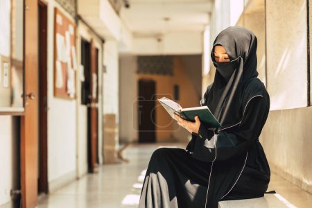 Photo for Young teen muslim niqab woman reading the Quran and faith The Holy Al Quran in University building. Arab black chador lady. - Royalty Free Image