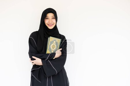 Retrato feliz musulmán saudita niqab árabe mujer chador negro con el libro de El Sagrado Corán aislado en blanco. portada del libro caligrafía árabe traducida a Al Corán