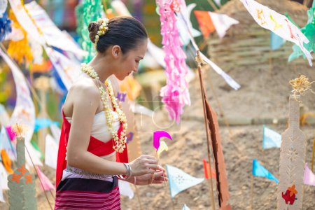 Téléchargez les photos : Festival de Songkran. Peuple thaïlandais du Nord habillé de vêtements traditionnels portant du sable dans le temple pour construire une pagode de sable et la décoration avec drapeau en papier coloré. - en image libre de droit