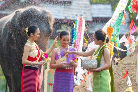 Téléchargez les photos : Festival de Songkran. Peuple thaïlandais du Nord en vêtements traditionnels s'habiller éclaboussant l'eau ensemble dans le festival culturel de jour de Songkran avec fond d'éléphant. - en image libre de droit