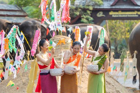 Téléchargez les photos : Festival de Songkran. Peuple thaïlandais du Nord en vêtements traditionnels s'habillant éclaboussant l'eau ensemble dans le festival culturel de jour de Songkran avec la pagode de sable et le drapeau coloré de papier. - en image libre de droit