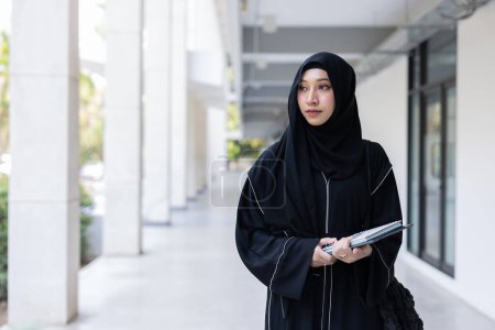 Université saoudienne musulmane niqab femme de l'enseignement supérieur dans le bâtiment du campus universitaire avec des livres de connaissances modernes. arabe saoudi noir chador adolescent dame.