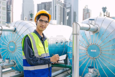 portrait asian male engineer worker work on site service maintenance hot water tank at roof top outdoor hotel building.