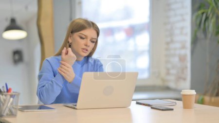 Téléchargez les photos : Jeune femme ayant la douleur au poignet tout en utilisant un ordinateur portable - en image libre de droit