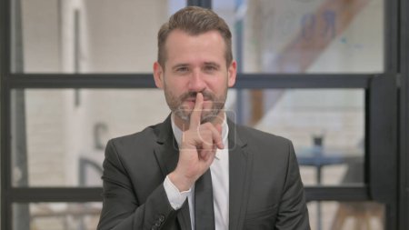 Porträt eines Geschäftsmannes mittleren Alters mit dem Finger auf den Lippen, bitte schweigen