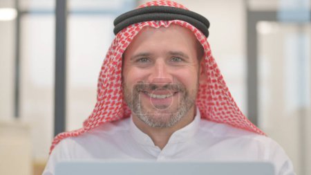 Primer plano del hombre árabe sonriente mientras trabaja en el ordenador portátil