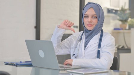 Pulgar hacia abajo por musulmana médico femenino mientras se trabaja en el ordenador portátil