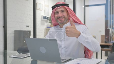 Hombre musulmán de mediana edad haciendo pulgares en cámara con ambas manos
