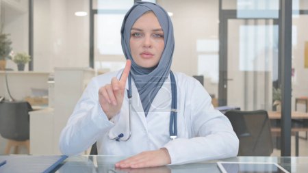 Médico en Hijab agitando la cabeza y el dedo en la negación